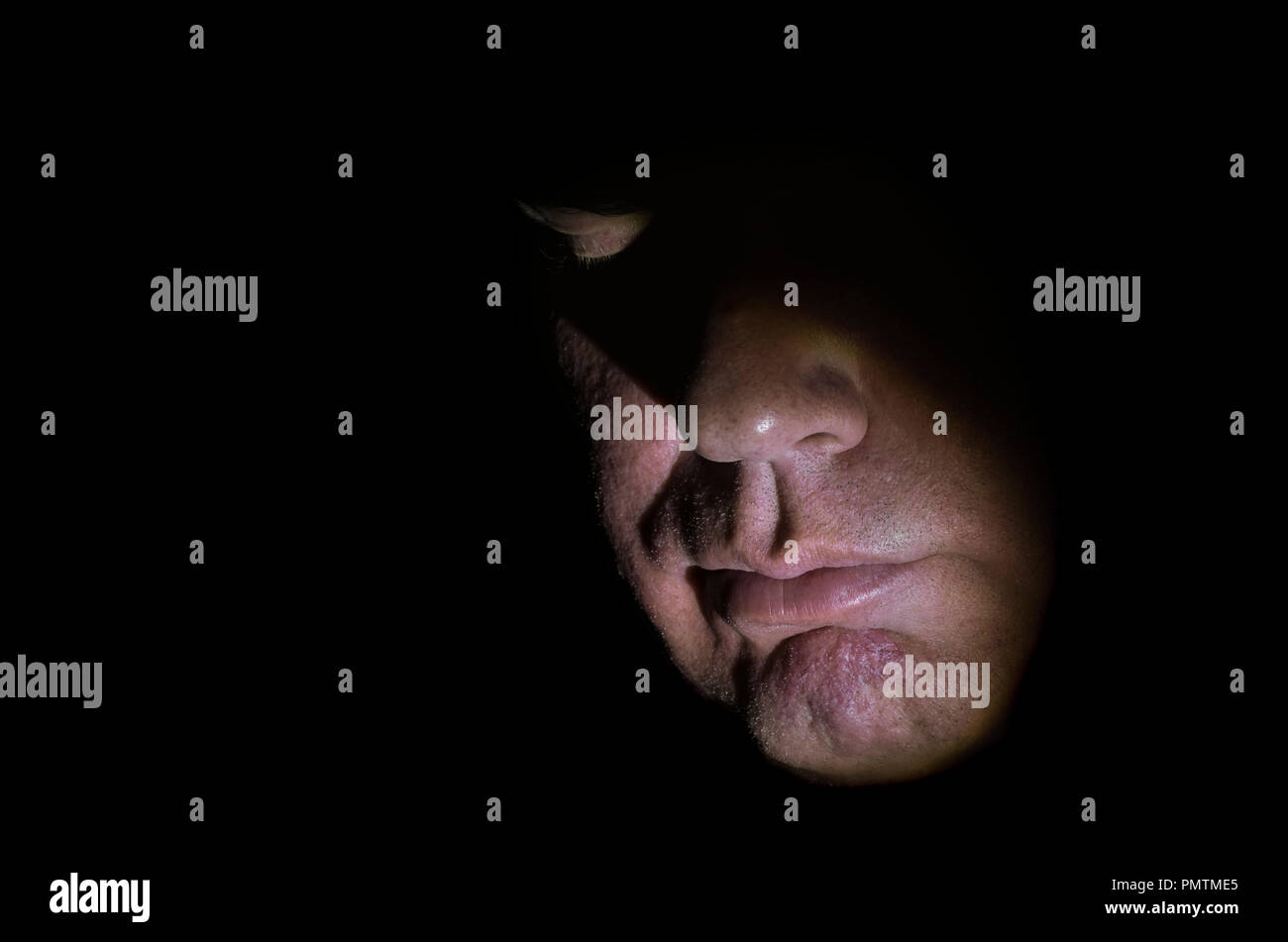 Modelo liberado closeup imagen de mediana edad del rostro del hombre caucásico, parcialmente iluminado con luces regulables y los ojos cerrados, mostrando la nariz y la boca, mirando hacia abajo. Foto de stock