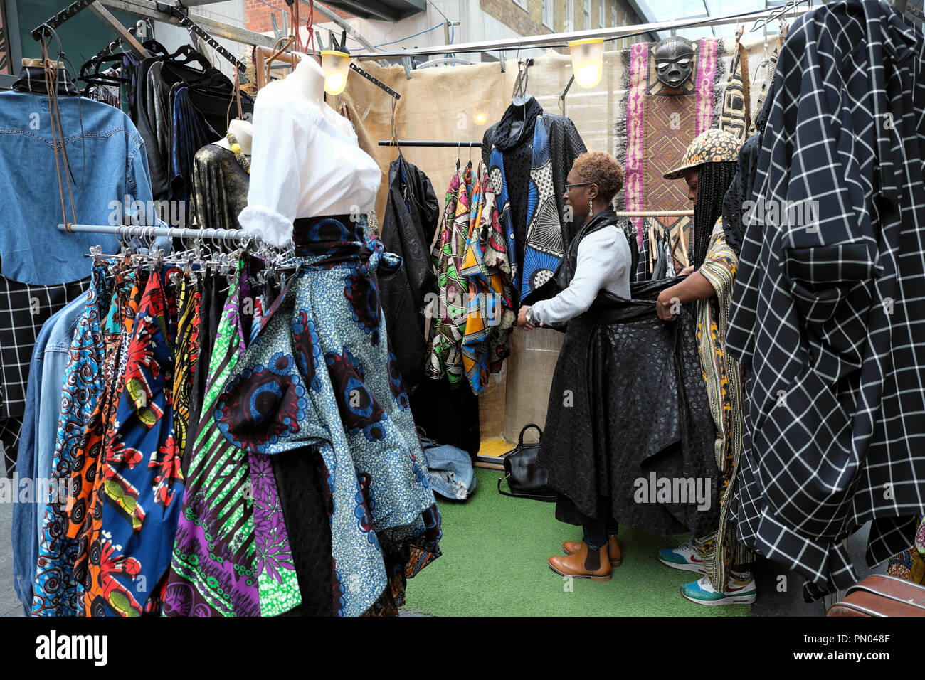 Una mujer tratando de vestido en tienda de ropa venta de ropa de tejidos  textiles africanos en Spitalfields Market, en East London, Reino Unido,  Kathy DEWITT Fotografía de stock - Alamy
