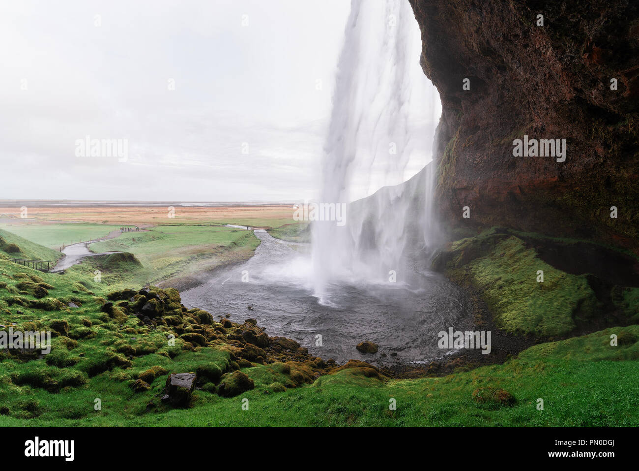 Cascada Seljalandsfoss y el camino que se extiende por todo el camino alrededor de ella. Rutas en los acantilados detrás de las cataratas Foto de stock