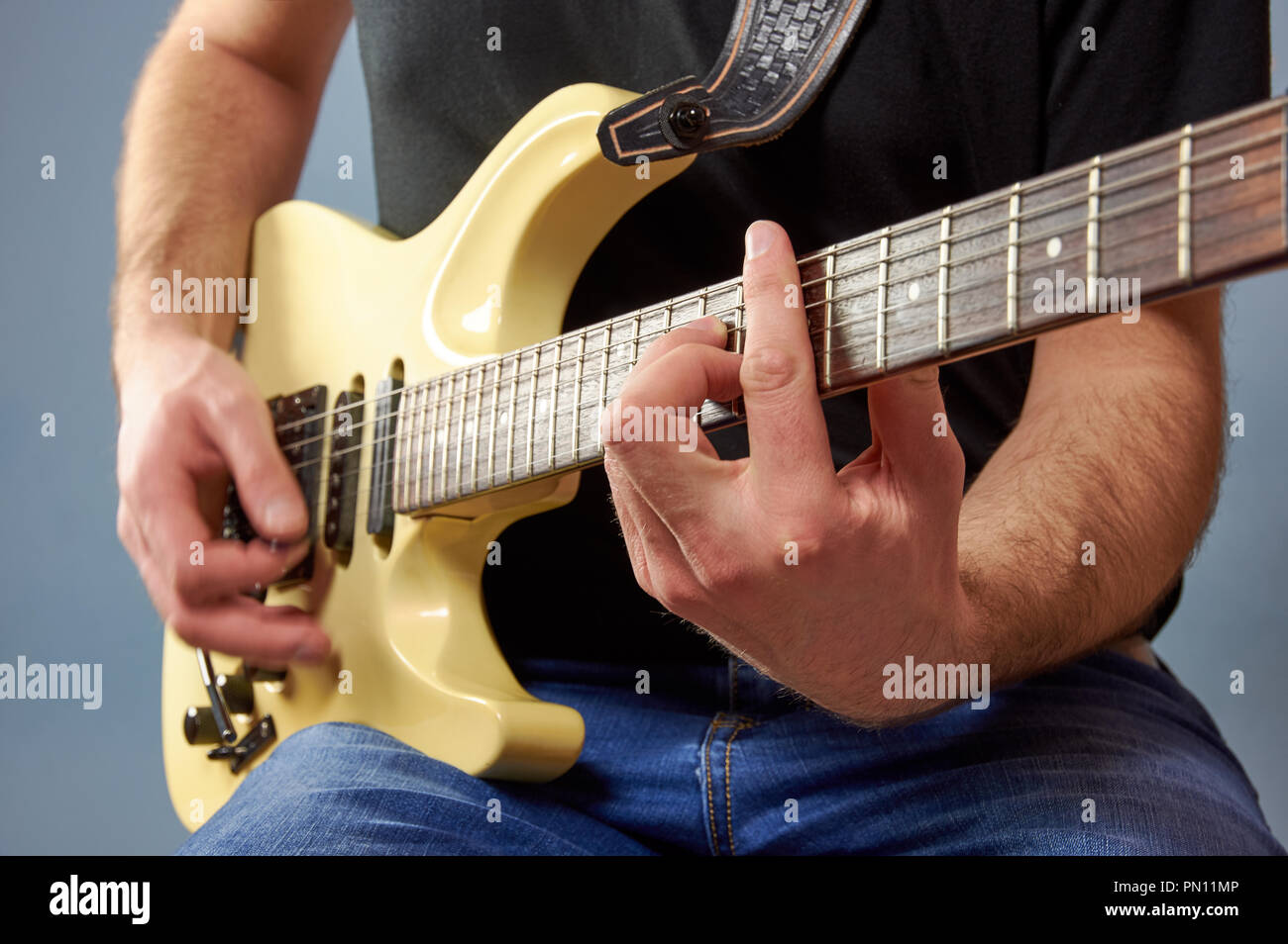 Un hombre en una camisa negra y jeans tocar una guitarra eléctrica. Detalle  de los dedos, fondo azul Fotografía de stock - Alamy