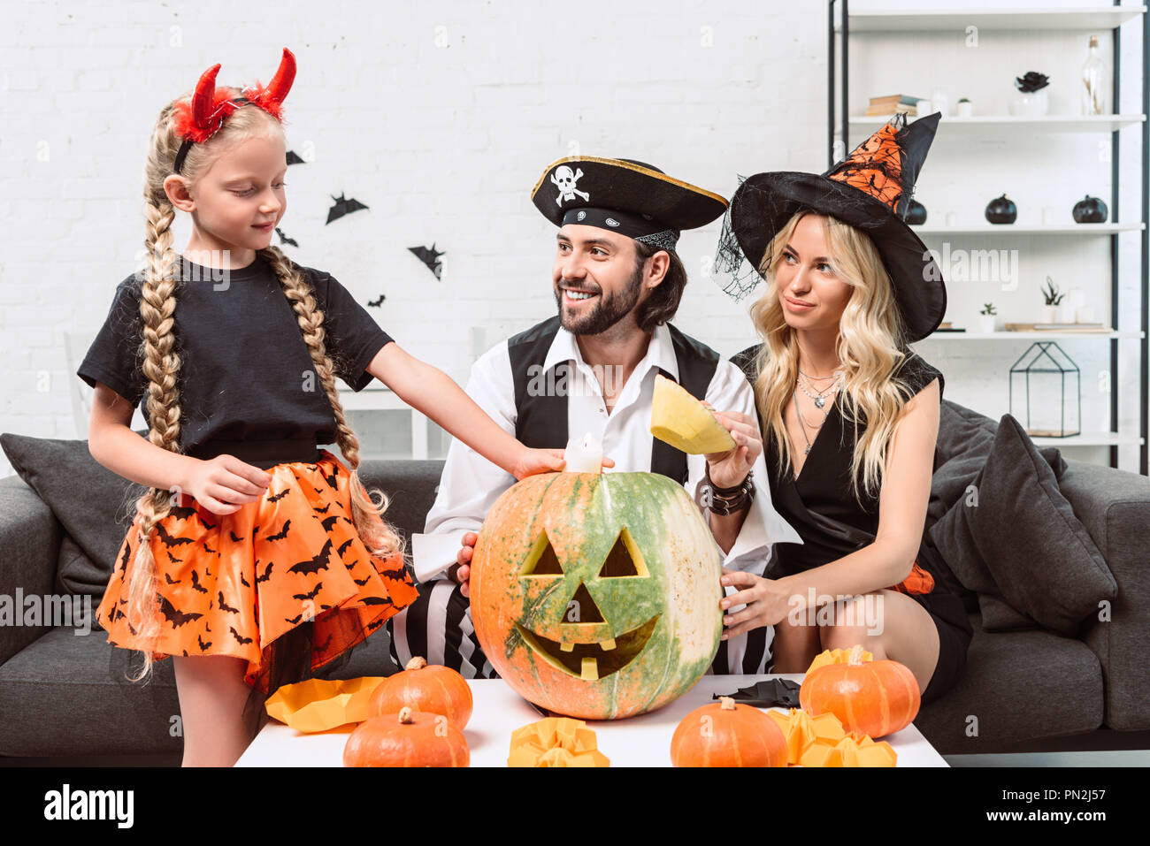 Familia en disfraces de Halloween en el sofá y mesa de café con calabazas  en casa Fotografía de stock - Alamy