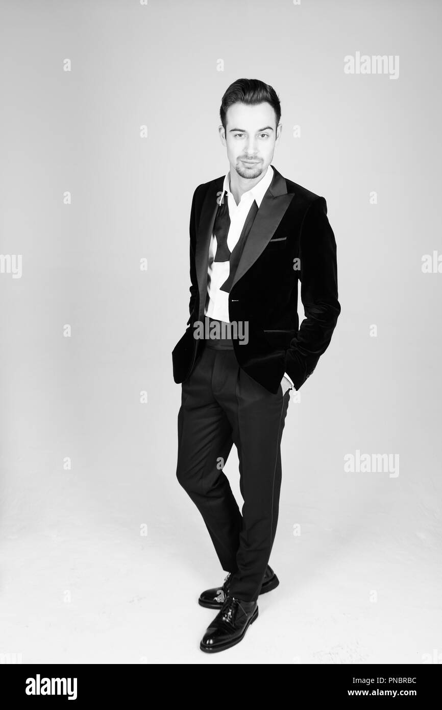 Retrato de un joven apuesto hombre en un traje, de pie y mirando a la  cámara, pajarita deshecha, contra la llanura fondo studio Fotografía de  stock - Alamy