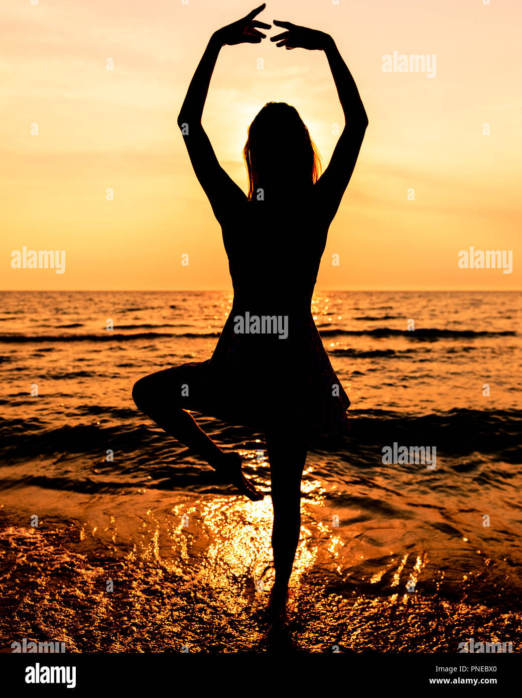 Jovencita en un vestido con pelo largo en la playa en silueta durante la puesta de sol en una pose de Ballet Foto de stock