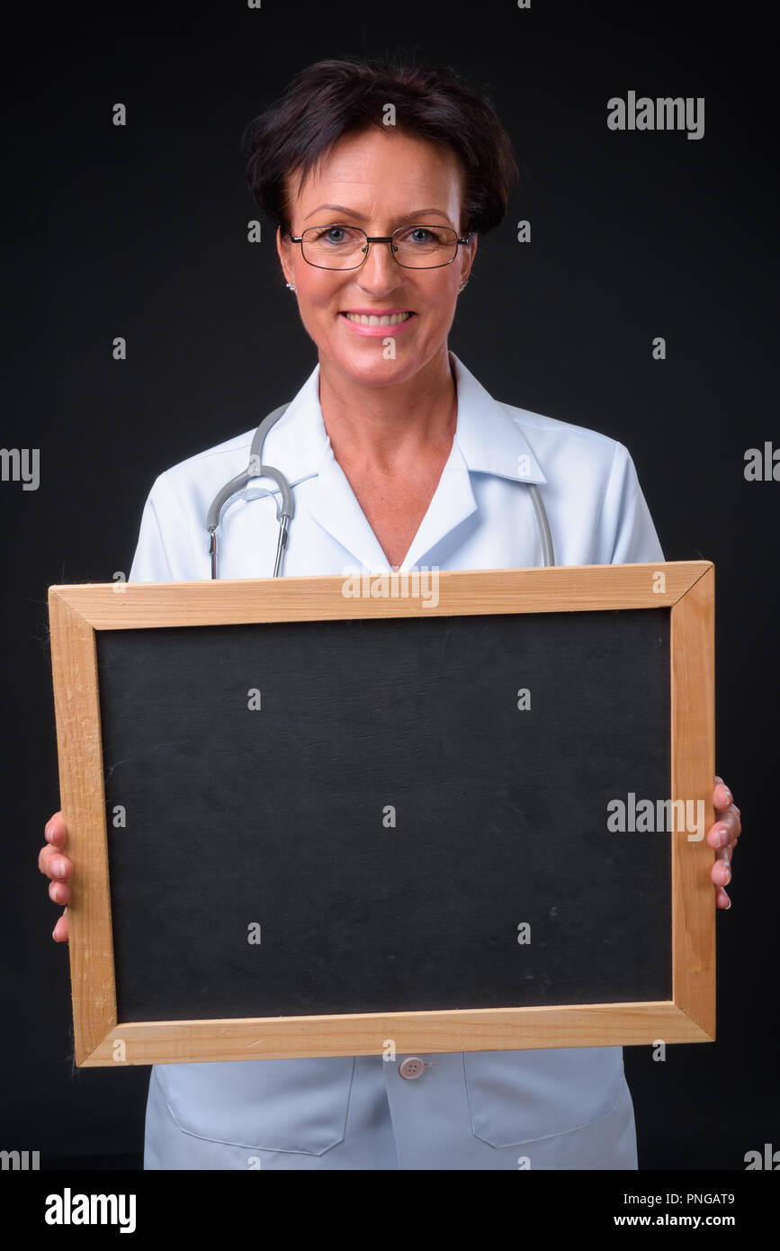 Hermosa mujer madura médico con pelo corto contra dorso negro Foto de stock