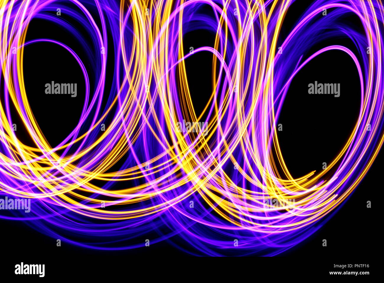 Fotografía, Pintura de luz larga exposición foto de violeta, rosa y oro las luces de hadas en abstracto bucles de luz contra un fondo negro Foto de stock