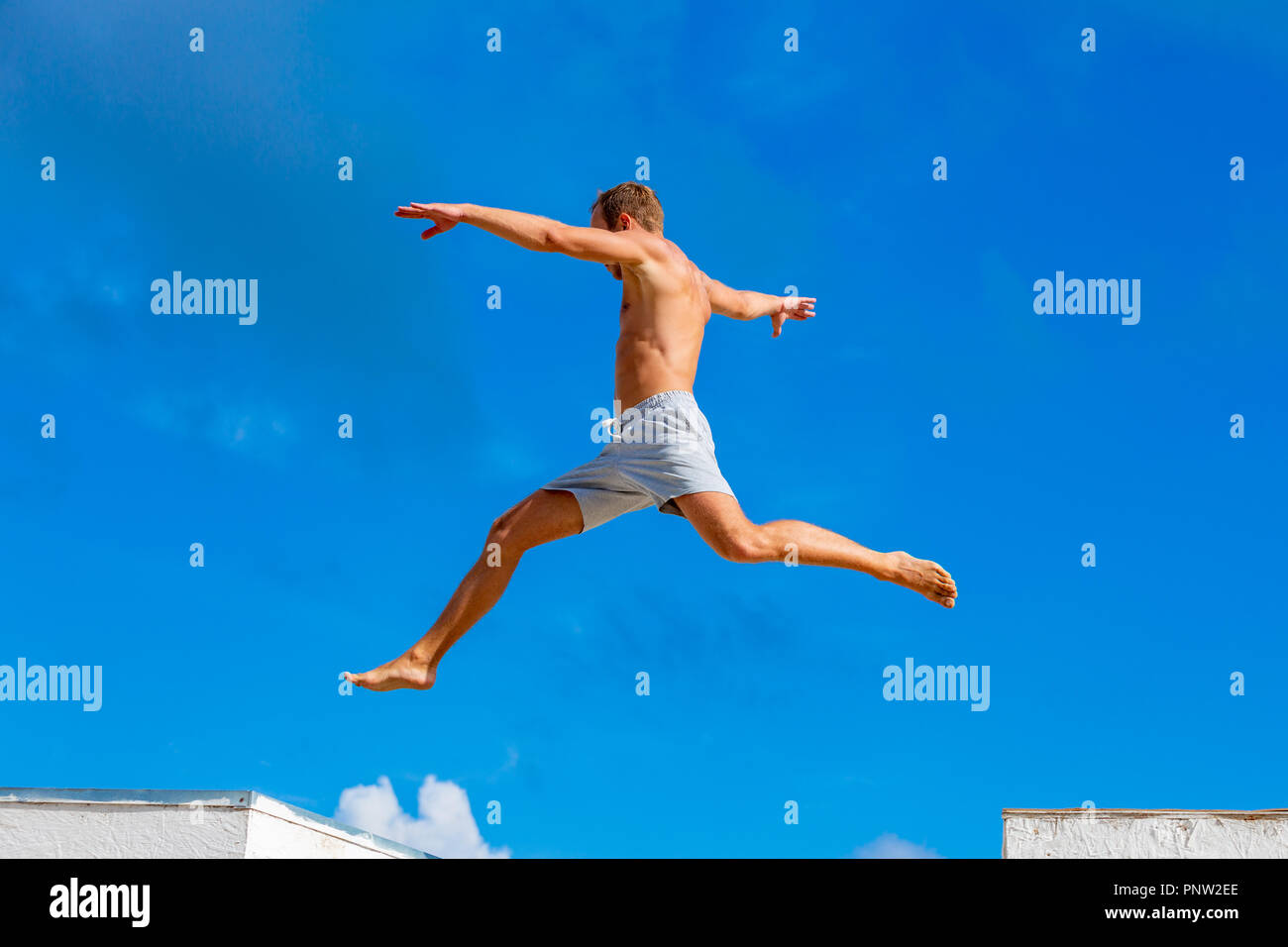 Joven haciendo parkour saltar sobre el fondo del cielo azul en un día soleado de verano Foto de stock