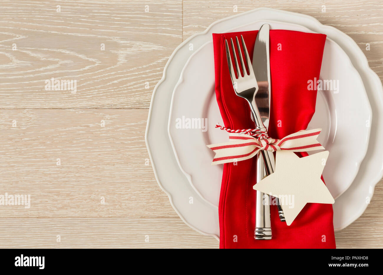 Ajuste de mesa navideños place setting con china blanca placas, una servilleta de tela de color rojo y plata sobre fondo de madera rústica. Horizontal con impedir Foto de stock