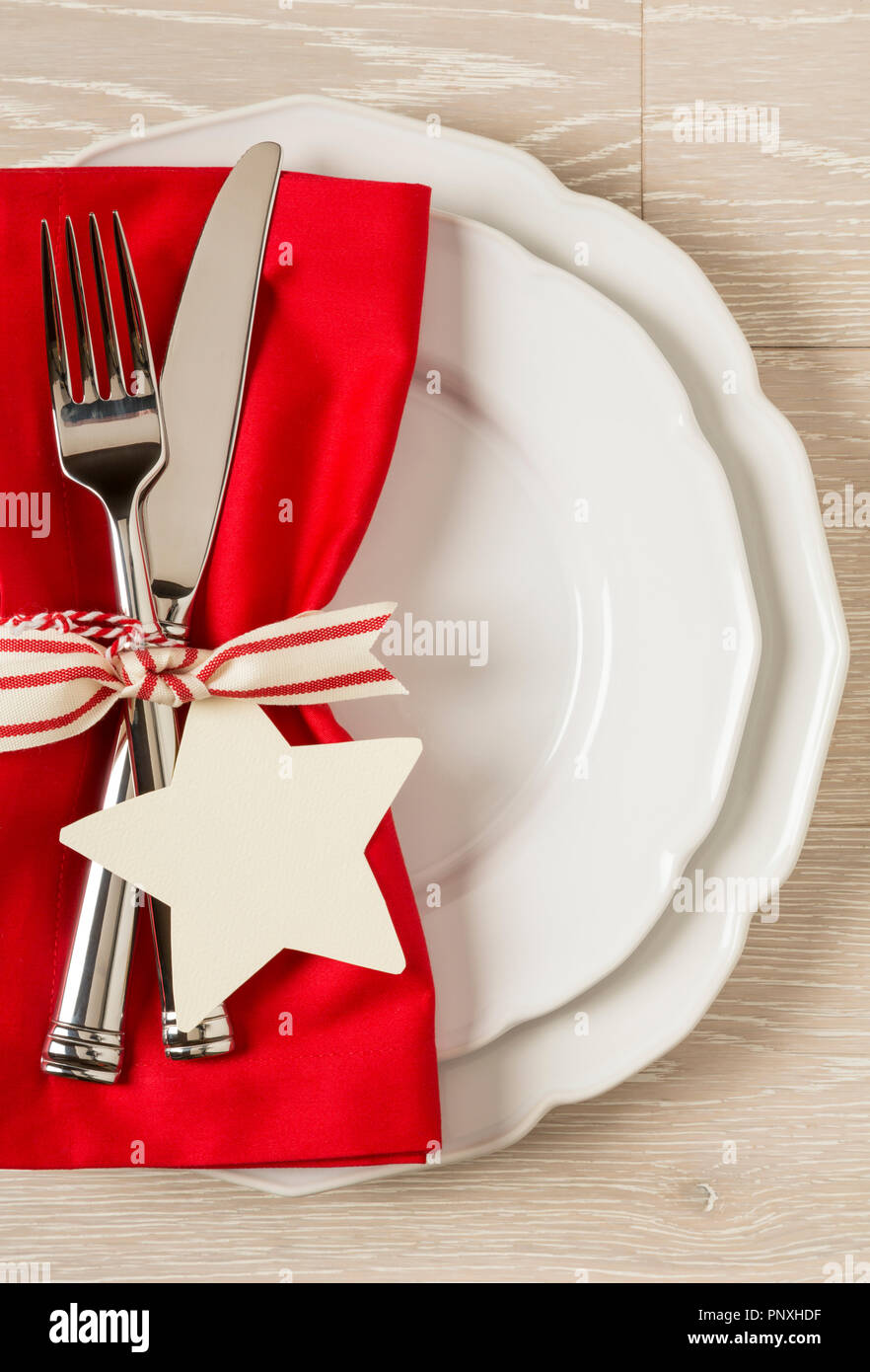 Ajuste de mesa navideños place setting con china blanca placas, una servilleta de tela de color rojo y plata sobre fondo de madera rústica. Vertical con vacío Foto de stock