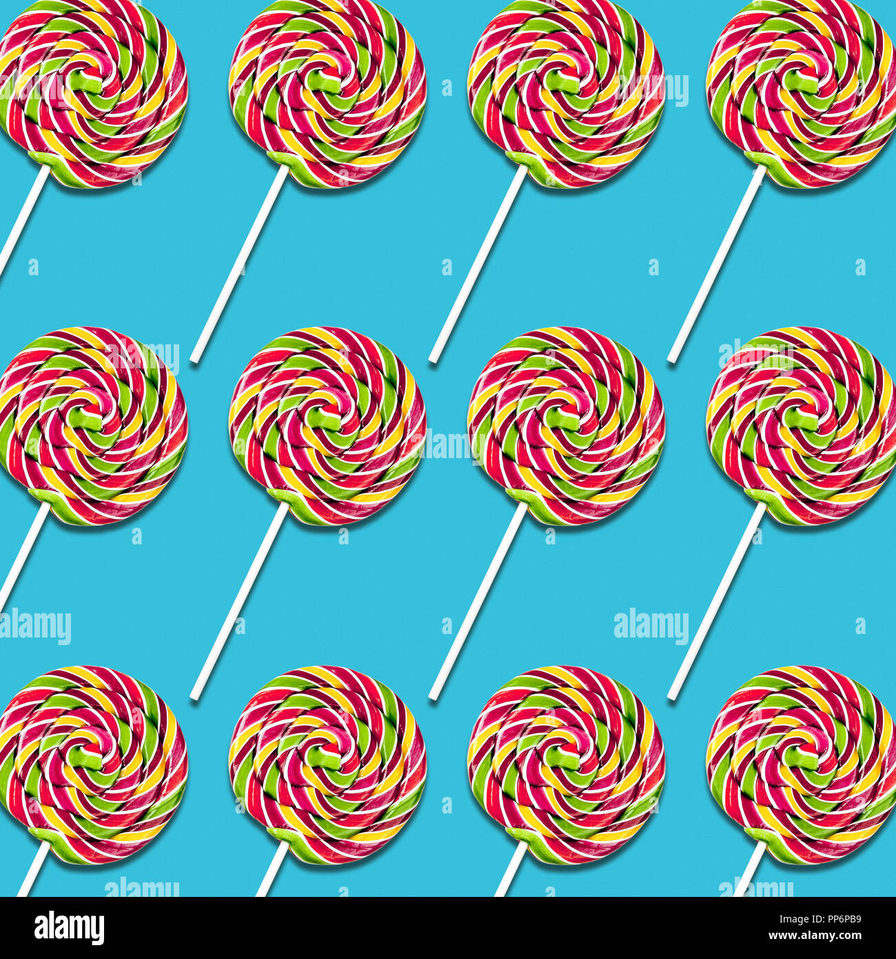 Disposición simétrica de lollipop caramelos sobre fondo turquesa, coloridos dulces de textura de alimentos Foto de stock