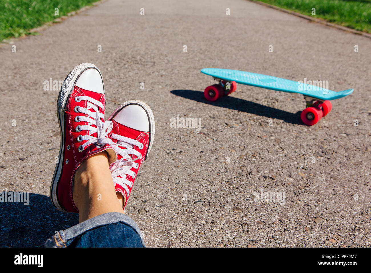 Cerca de los pies de una chica en zapatillas rojas y azules penny plástico  skate bordo de color rosa con ruedas en el fondo. Escena urbana, la vida en  la ciudad. Deporte,