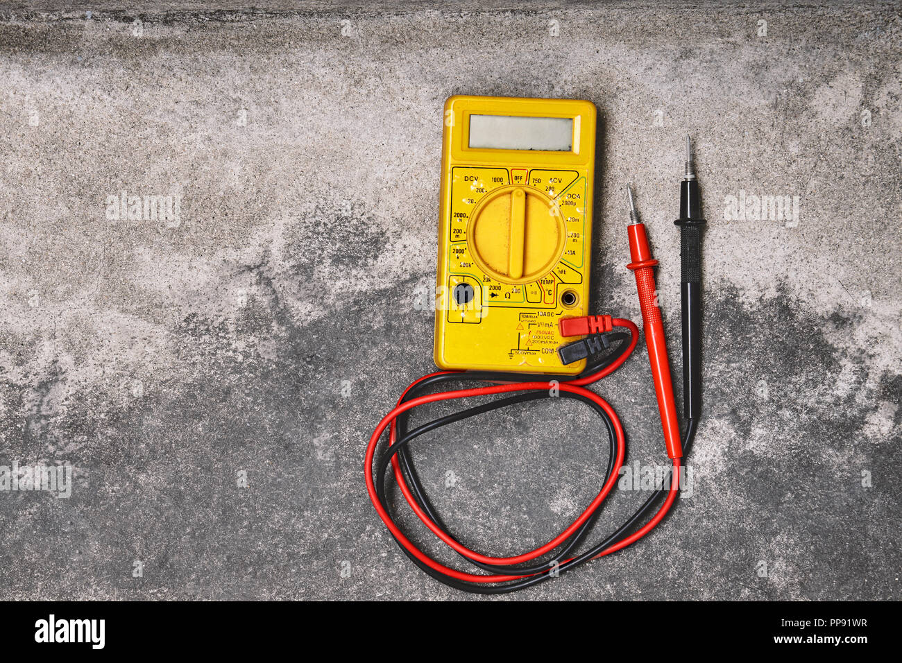 Bricolaje hogar electricidad herramientas de trabajo conceptos, antiguo multímetro amarillo sobre fondo de cemento polvoriento Foto de stock