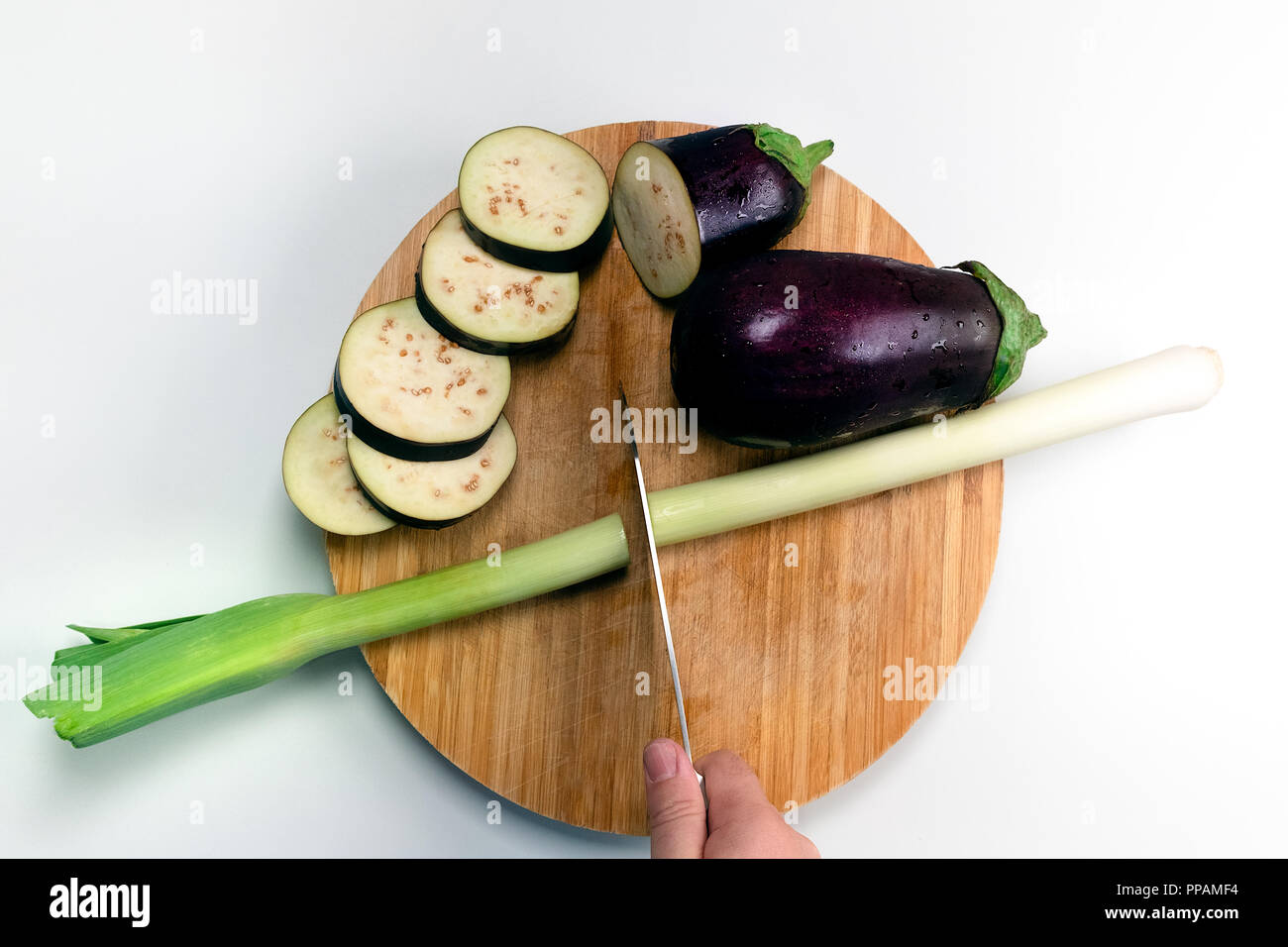 Puerro, cebolla y albahaca sobre una tabla para cortar, durante el tiempo de cocción. Foto de stock