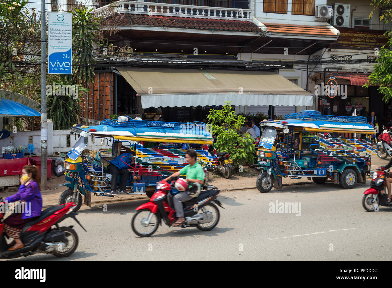 Motos y dos estacionaron coloridos taxis de tres ruedas llamado jumbo (o un tuk-tuk) en la calle Sisavangvong en Luang Prabang, Laos, en un día soleado. Foto de stock