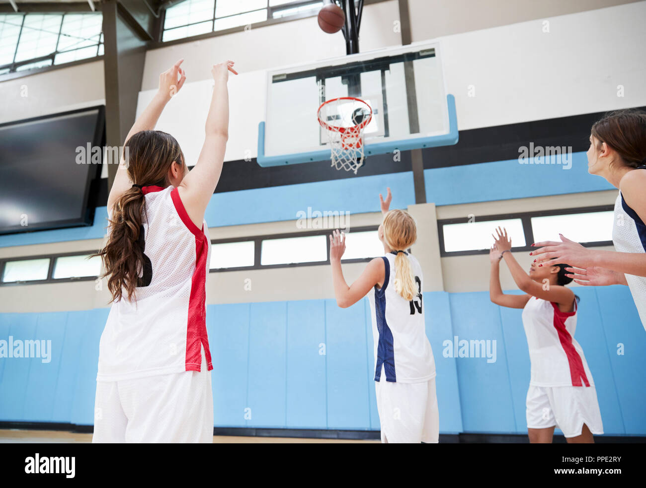 Equipo de baloncesto de la escuela secundaria femenina disparando a la cesta en la corte Foto de stock
