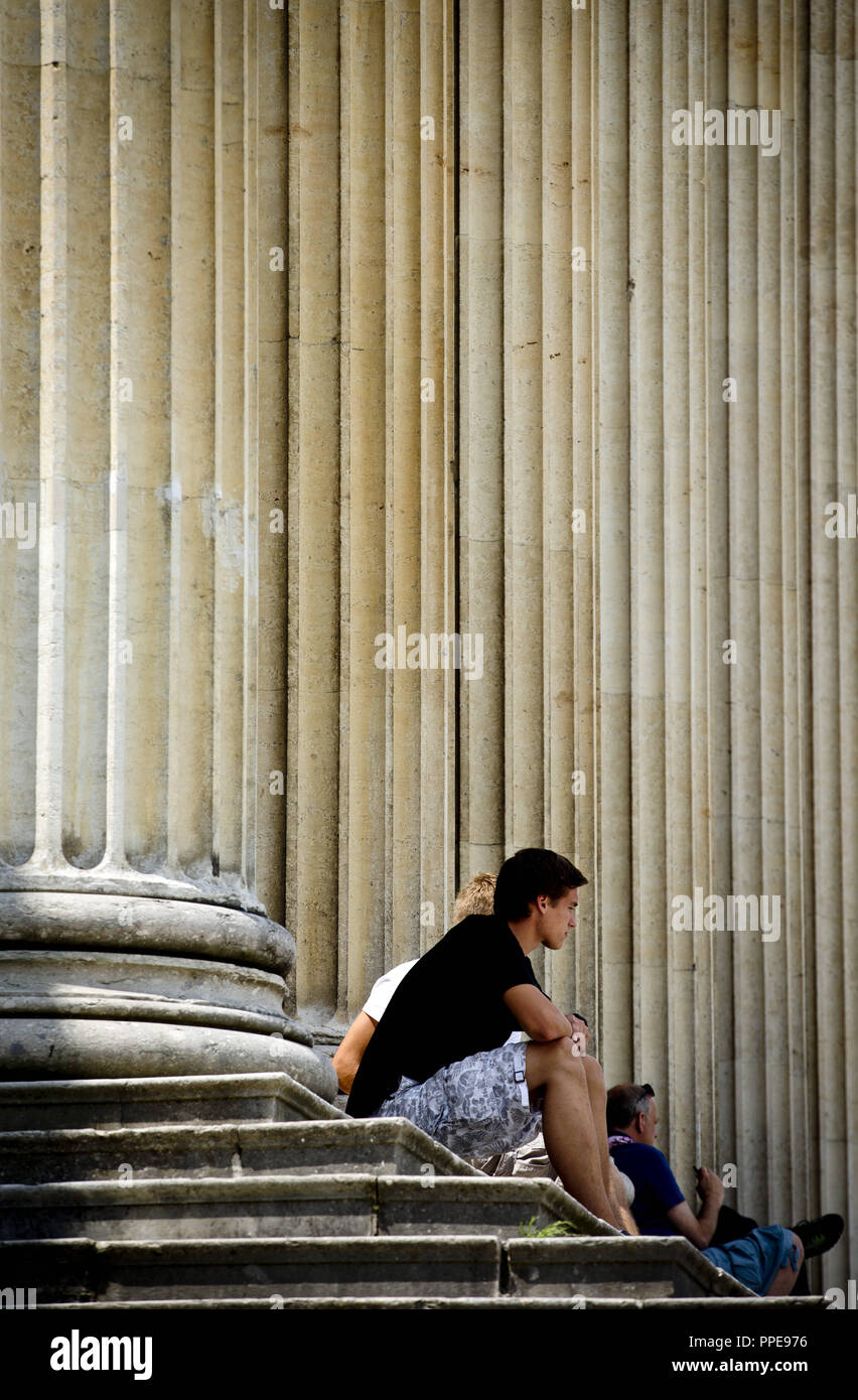 La gente sentada en los escalones entre las columnas de la Staatliche Antikensammlungen (Estado) en colecciones de antigüedades Koenigsplatz en Munich. Foto de stock