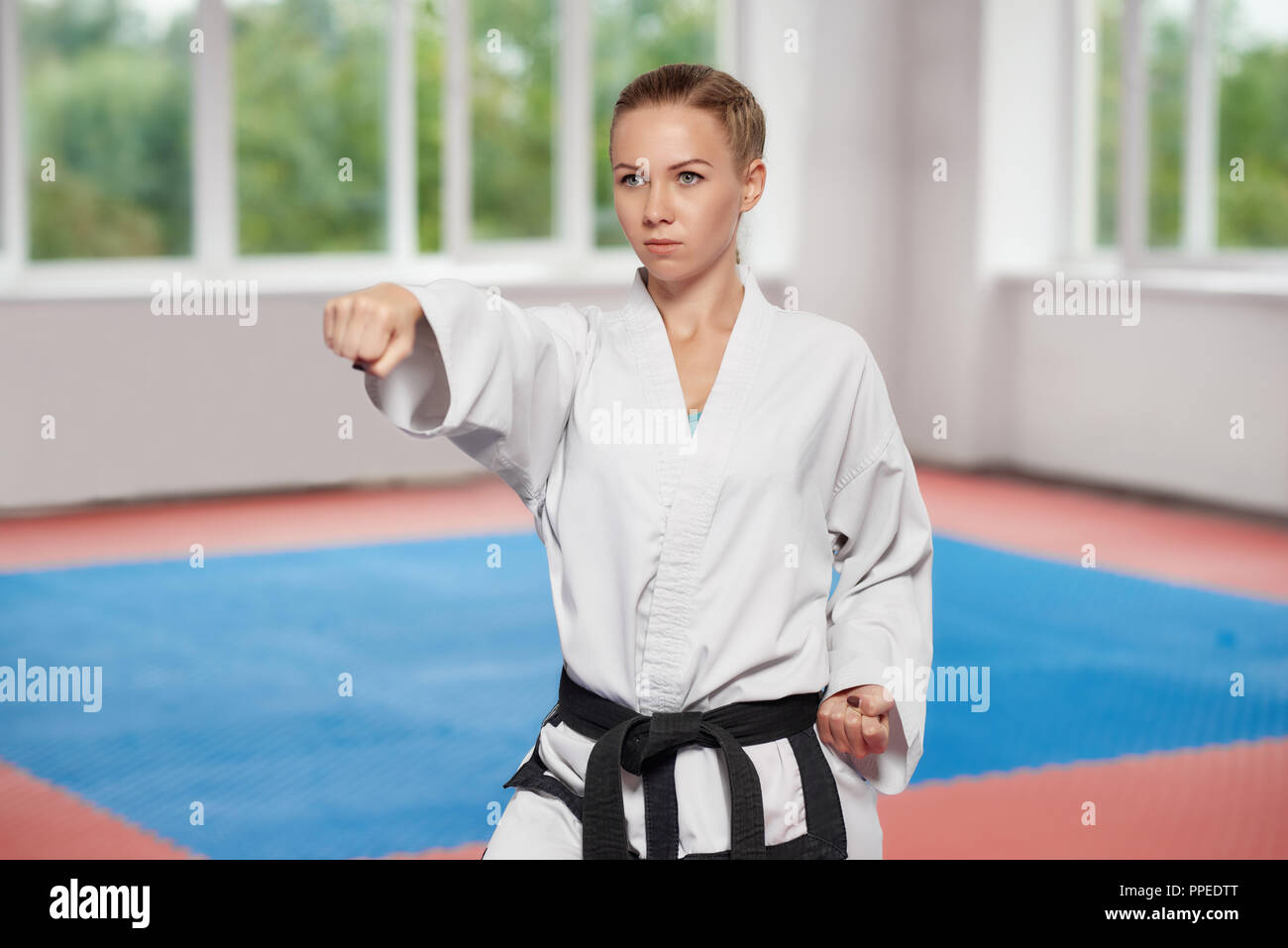 Fuerte joven vestida en kimono blanco con cinturón negro en karate  permanente plantean en brillante clase de karate. Combatiente femenino con  ojos azules y pelo trenzado seriamente buscando recto con puño Fotografía