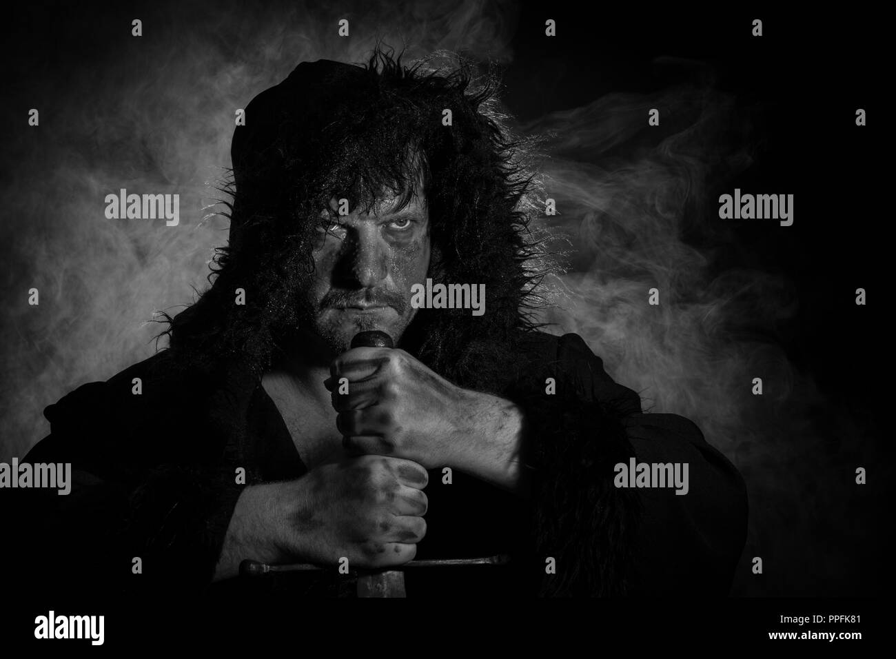 Hombre con capucha, puños cerrados y la espada delante de la niebla, la mirada combativa, Alemania Foto de stock