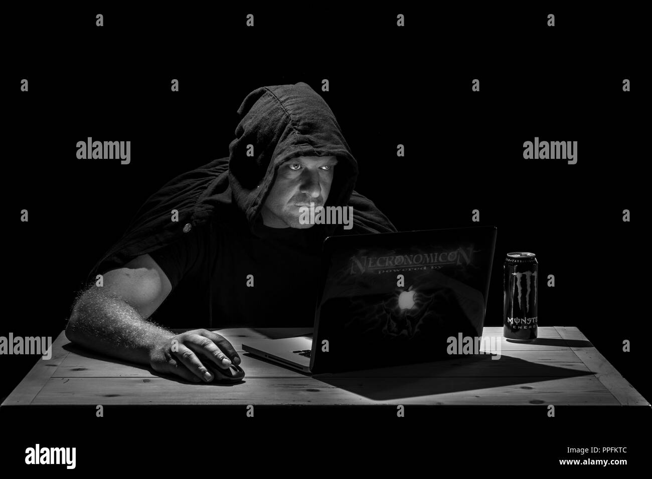 El hombre está sentado a la mesa en una habitación oscura, mirando en su portátil, símbolo imagen para hacker, ciberdelincuencia, Alemania Foto de stock