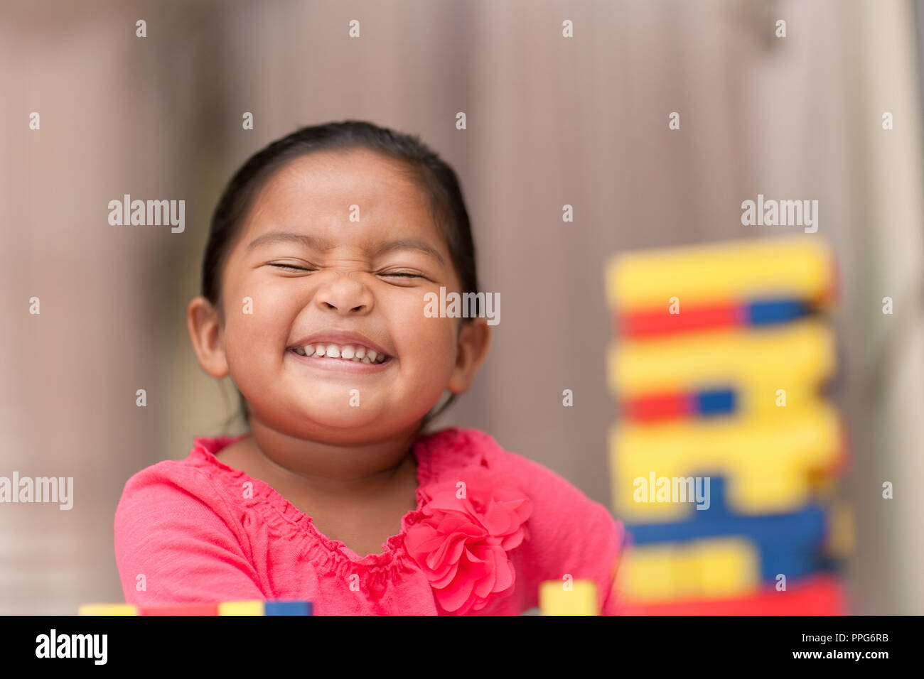 Latino sonriente niña jugando con coloridos bloques de construcción que se siente orgulloso de sus logros Foto de stock