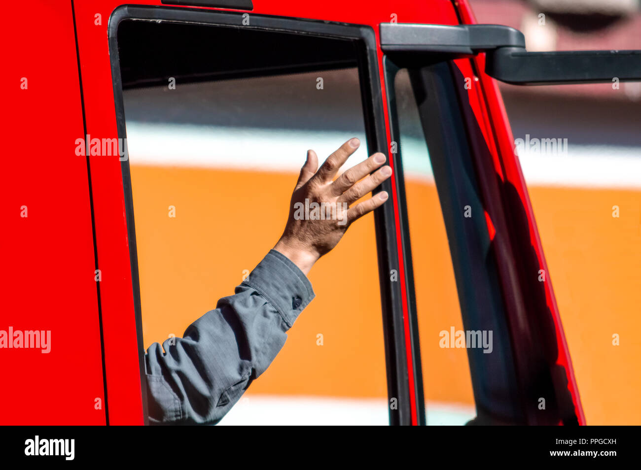 El brazo de una persona saludando desde la ventana de un camión rojo Foto de stock