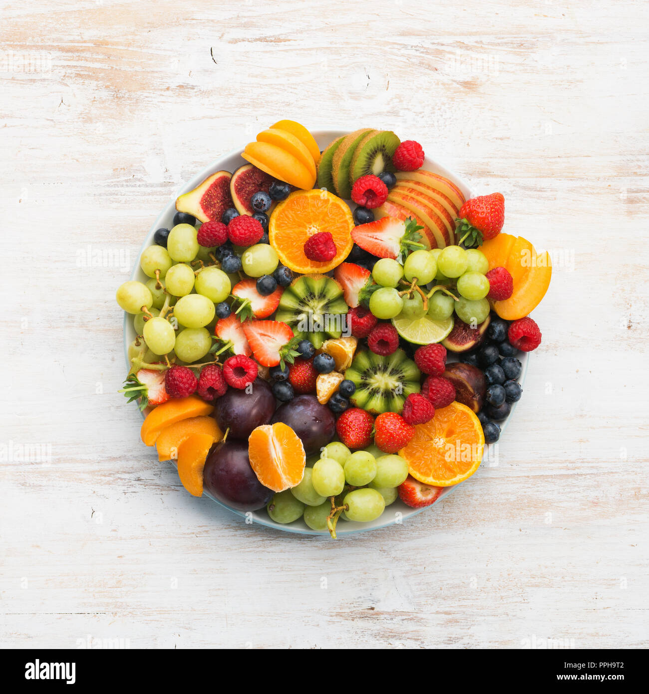 Plato de frutas saludables frambuesas, fresas, naranjas Ciruelas Kiwis Manzanas Uvas arándanos sobre la mesa de madera blanca, vista superior, espacio para copiar texto Foto de stock