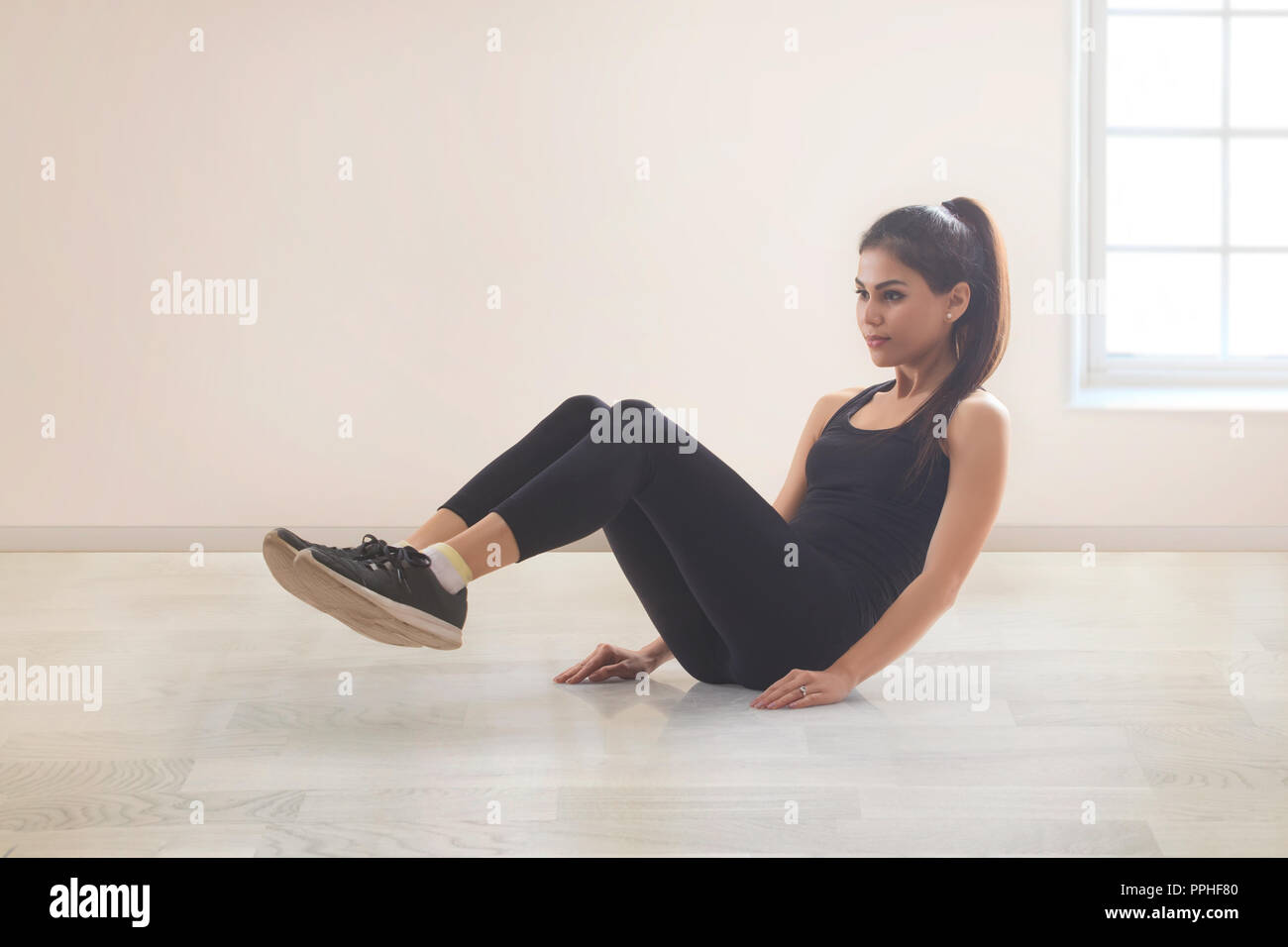 Mujer joven en ropa de entrenamiento haciendo ejercicios sobre el piso. Foto de stock