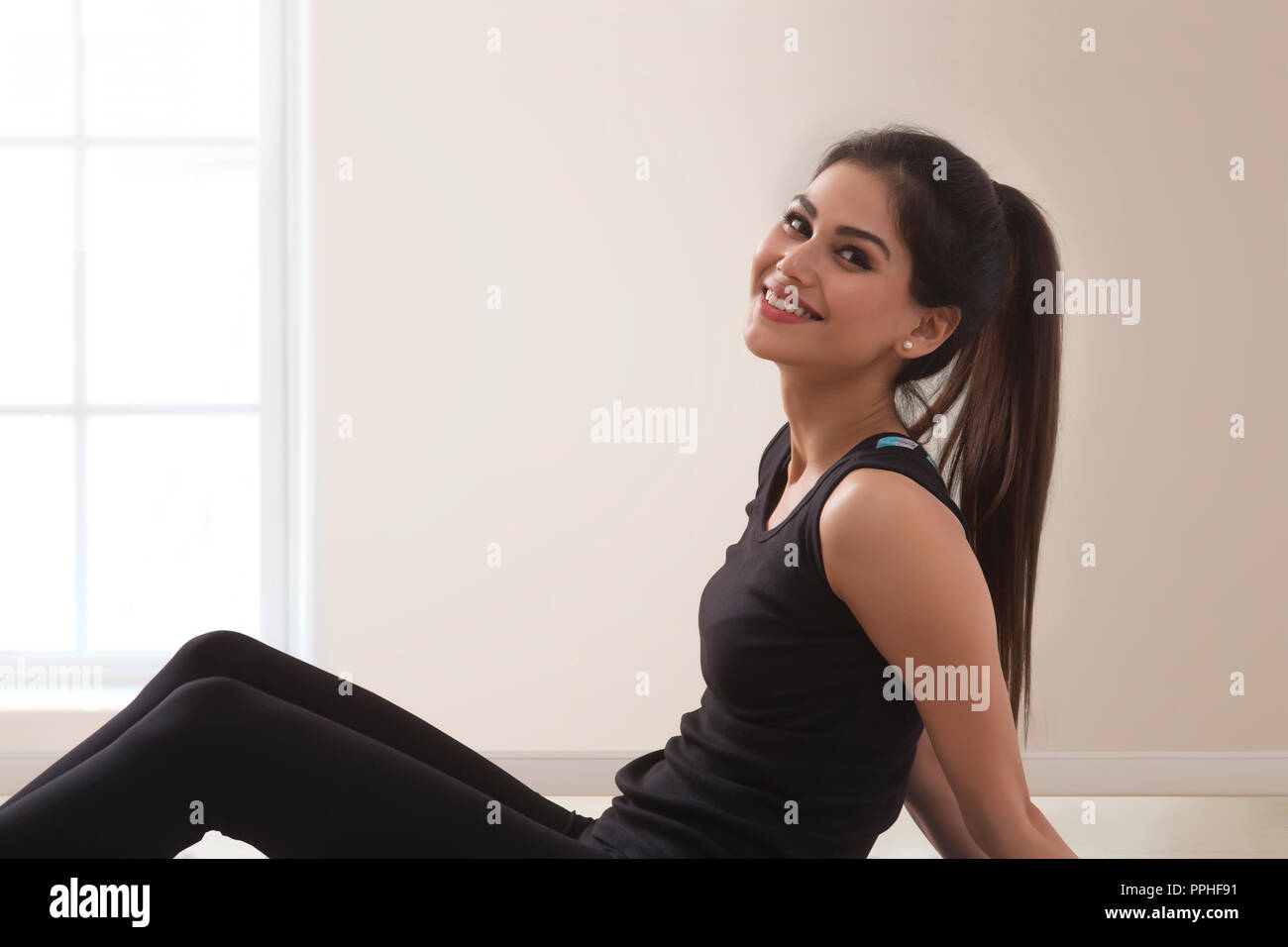 Cerca del joven sonriente mujer fitness en chándal haciendo yoga sentada en el suelo. Foto de stock
