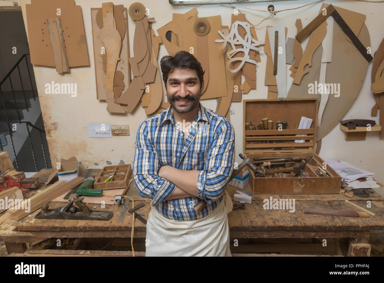 Retrato de carpintero en su taller permanente sosteniendo un martillo con los brazos cruzados. Foto de stock