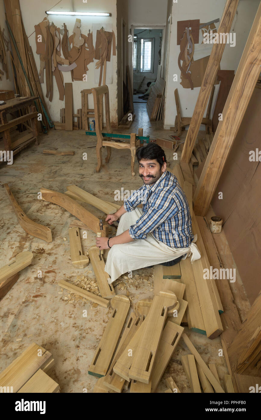 Sonriendo carpintero trabajando en madera con un cincel y un martillo sentado en su taller. Foto de stock
