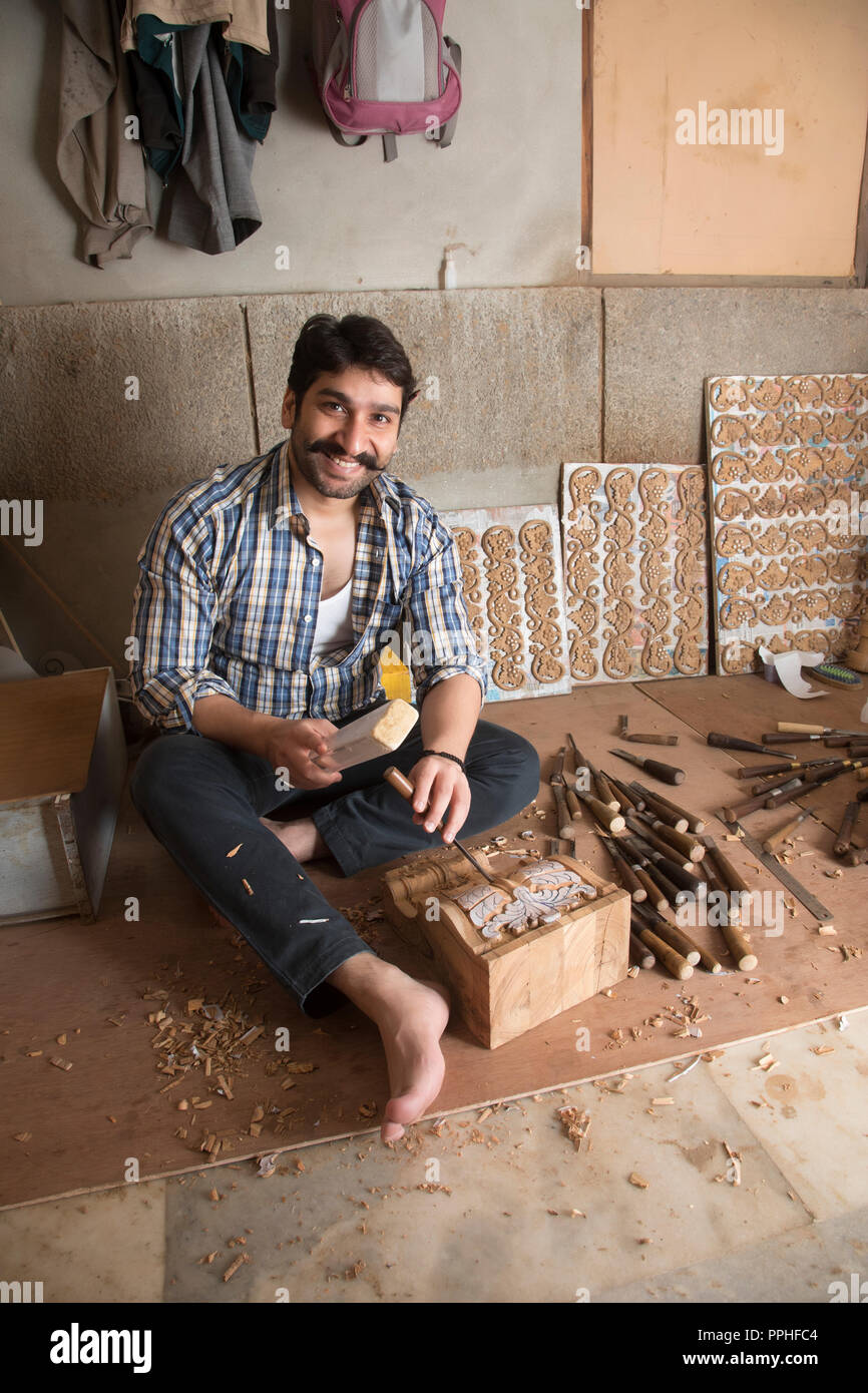 Carpintero sonriente haciendo esculturas y diseños en madera utilizando un cincel en su taller. Foto de stock