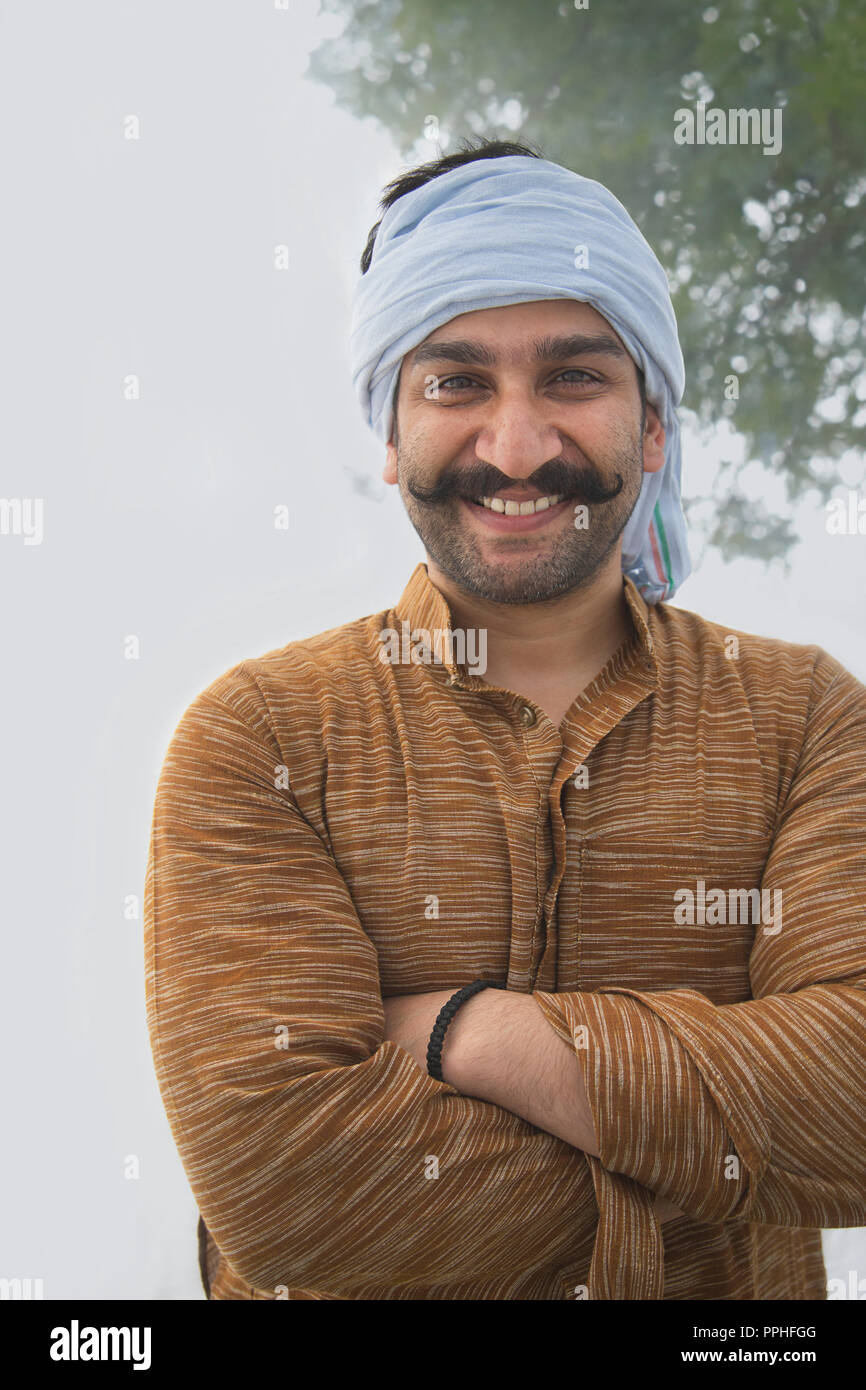Retrato de un hombre de la aldea sonriente haber rizado bigote de pie con los brazos cruzados con un turbante. Foto de stock