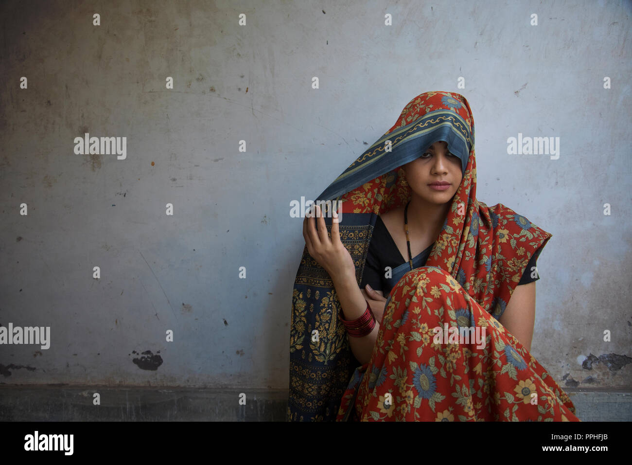 Primer plano de una bella mujer sentada en el suelo que cubre su cabeza con saree mirando hacia abajo. Foto de stock