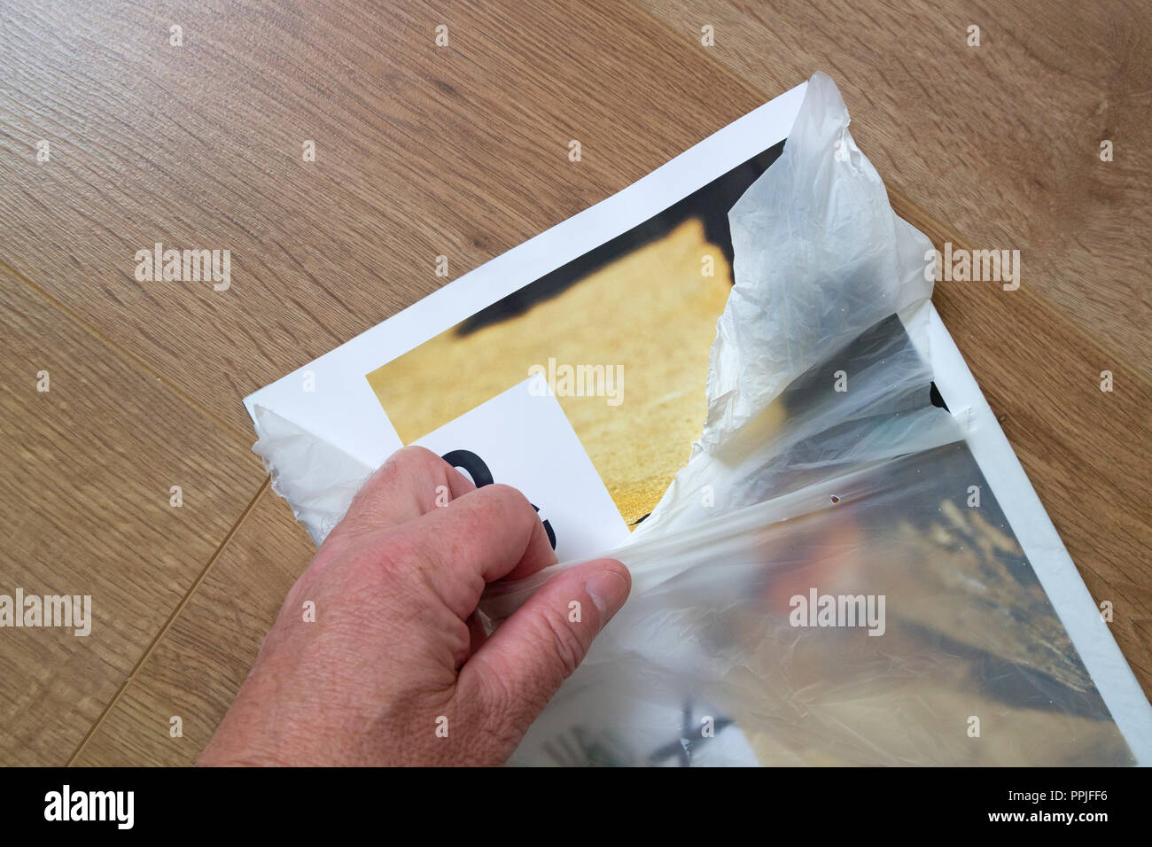 Persona lagrimeo abriendo una revista hecha de envoltura de plástico biodegradable de almidón de maíz, REINO UNIDO Foto de stock