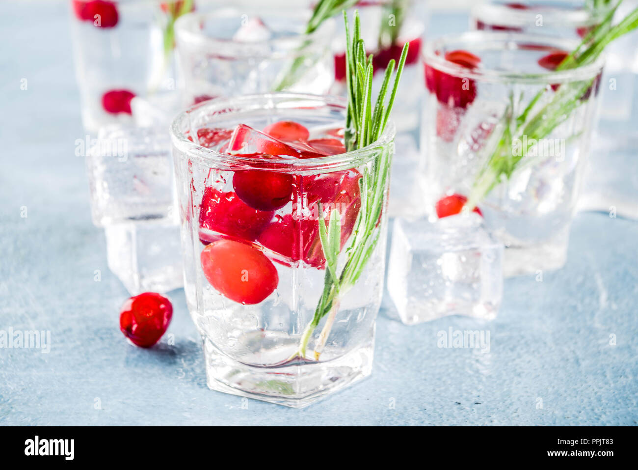 Navidad o Año Nuevo invierno cocktail de arándanos con romero, licores, gin tonic, sobre la luz azul de fondo de hormigón con cubitos de hielo, bayas frescas y Foto de stock