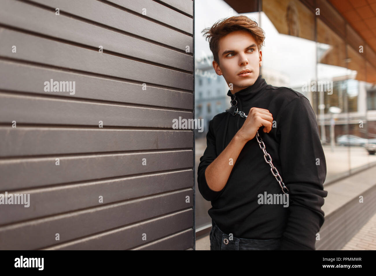 Apuesto joven en moda ropa negra con una bolsa plantea en la calle cerca de  la pared de madera Fotografía de stock - Alamy