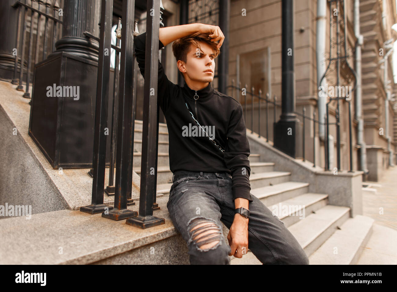 Moda Hombre en un modelo guapo negro moda jeans pullover con sentarse cerca  de una casa en la calle Fotografía de stock - Alamy