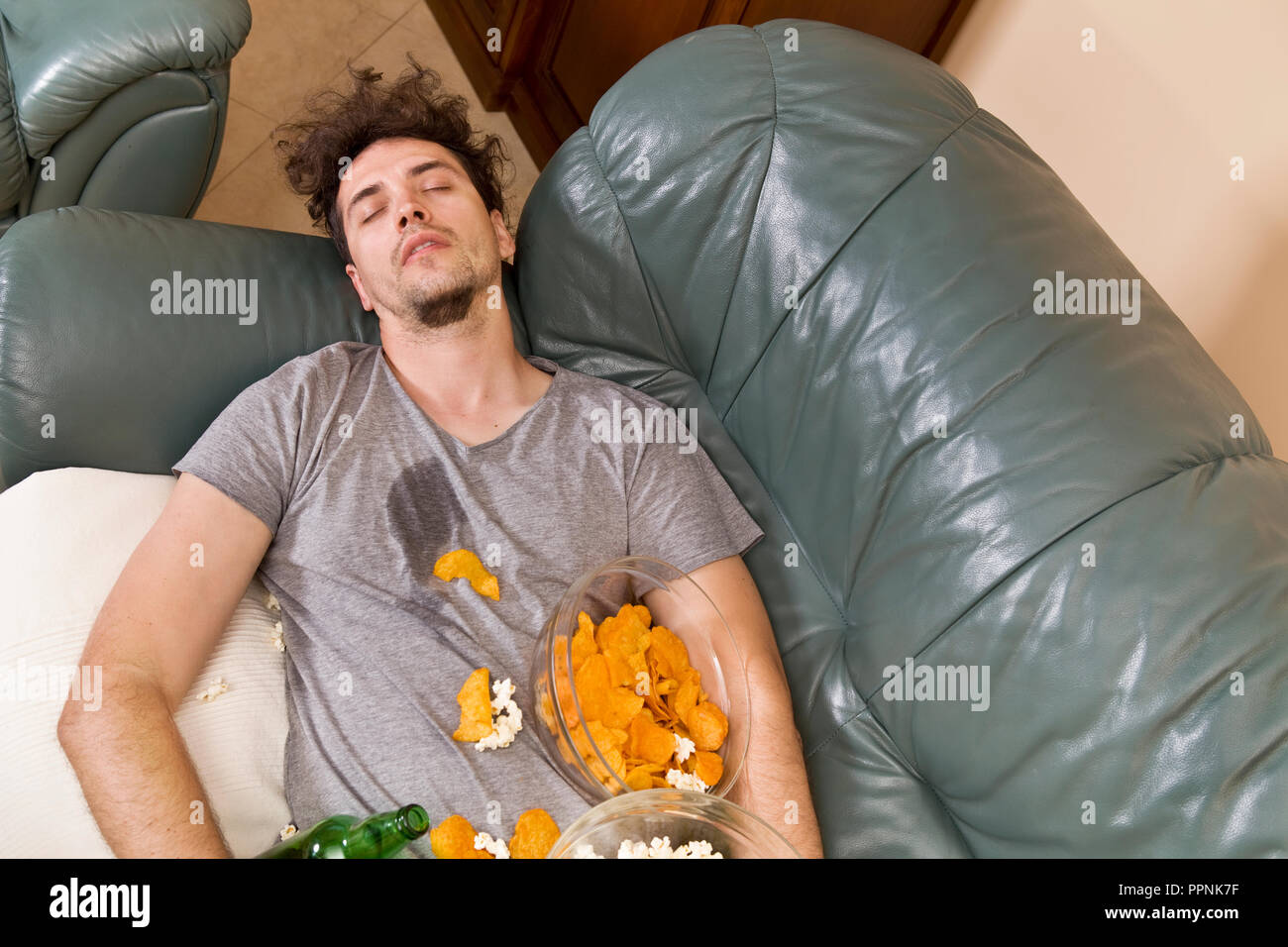 Cansado joven durmiendo en un sofá con la comida después de parte Foto de stock