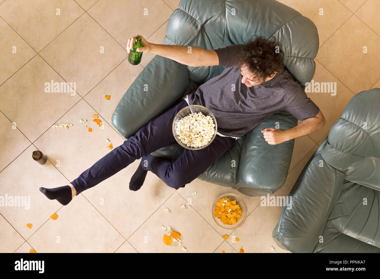 Vista superior del hombre con cerveza y patatas fritas y palomitas viendo la televisión en casa Foto de stock