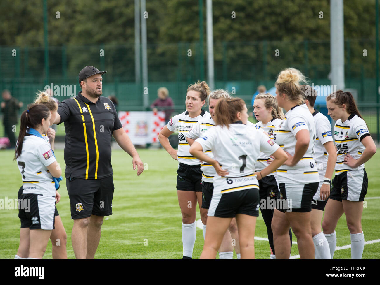 Un grupo de jugadores de rugby femenino escuchando a su entrenador hablar las tácticas de equipo durante un descanso de medio tiempo en un partido de rugby. Foto de stock