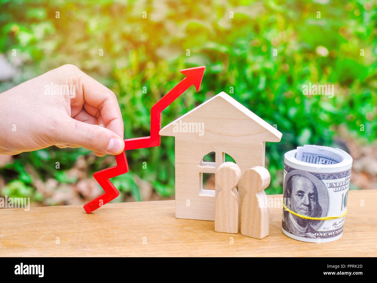 Casa de madera, el dinero con una flecha roja. Concepto de alta demanda para bienes raíces. La subida de los precios de la vivienda. El crecimiento de la población. El incremento en el coste del util Foto de stock