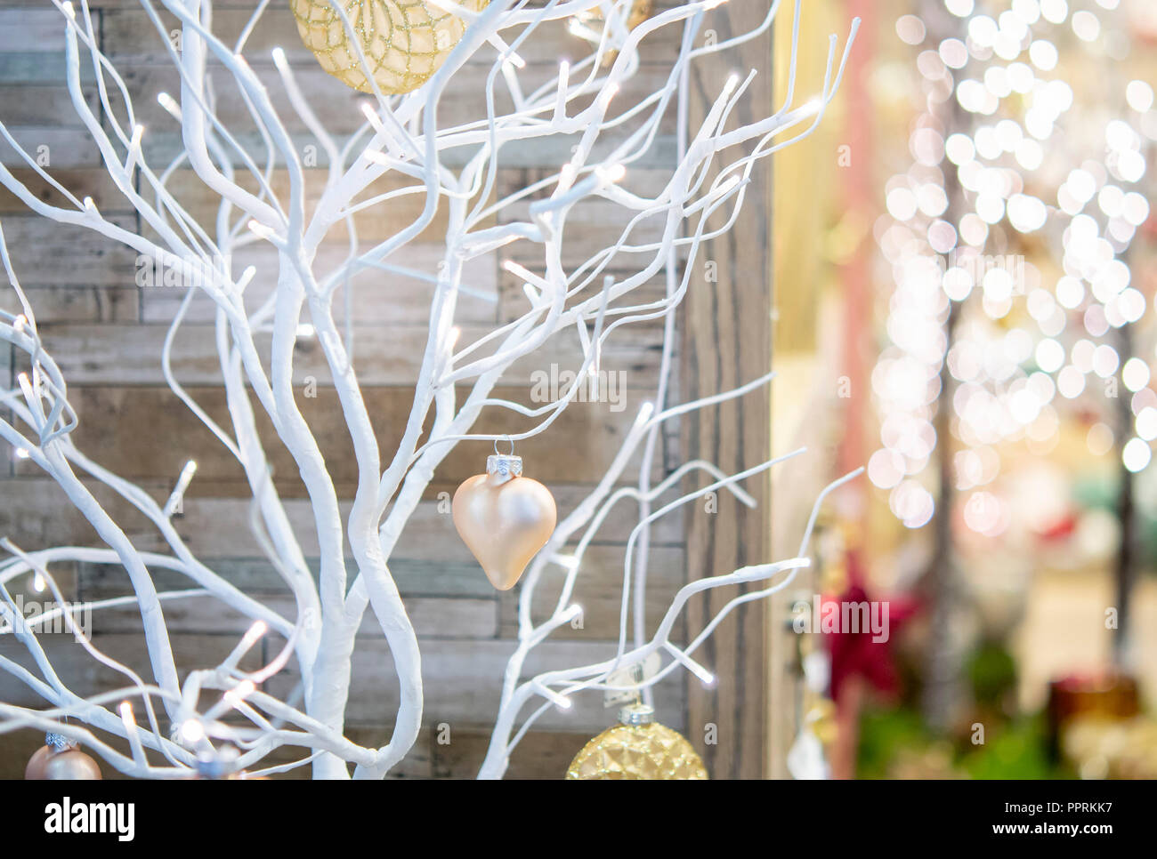Pequeño árbol seco pintado en color blanco decorado con juguetes decorativos corazón durante una nevada de cerca en el interior de la casa. Navidad Año Nuevo invierno paisaje de fondo. Concepto Foto de stock