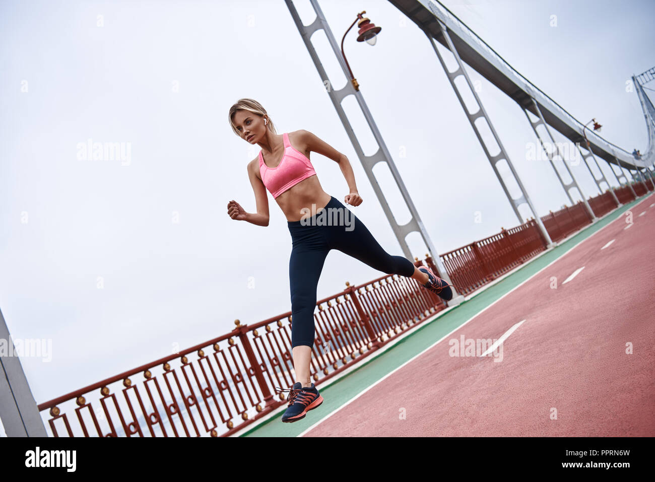 Ejercicios matutinos. Cerca de jóvenes womanin ropa deportiva hacer ejercicio mientras jogging en el puente al aire libre Foto de stock