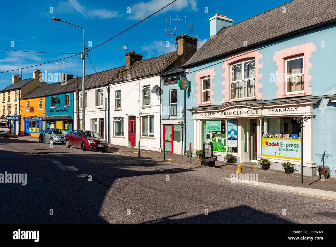 Coloridas casas y tiendas en la calle principal, Drimoleague, West Cork, Irlanda, en un día soleado. Foto de stock