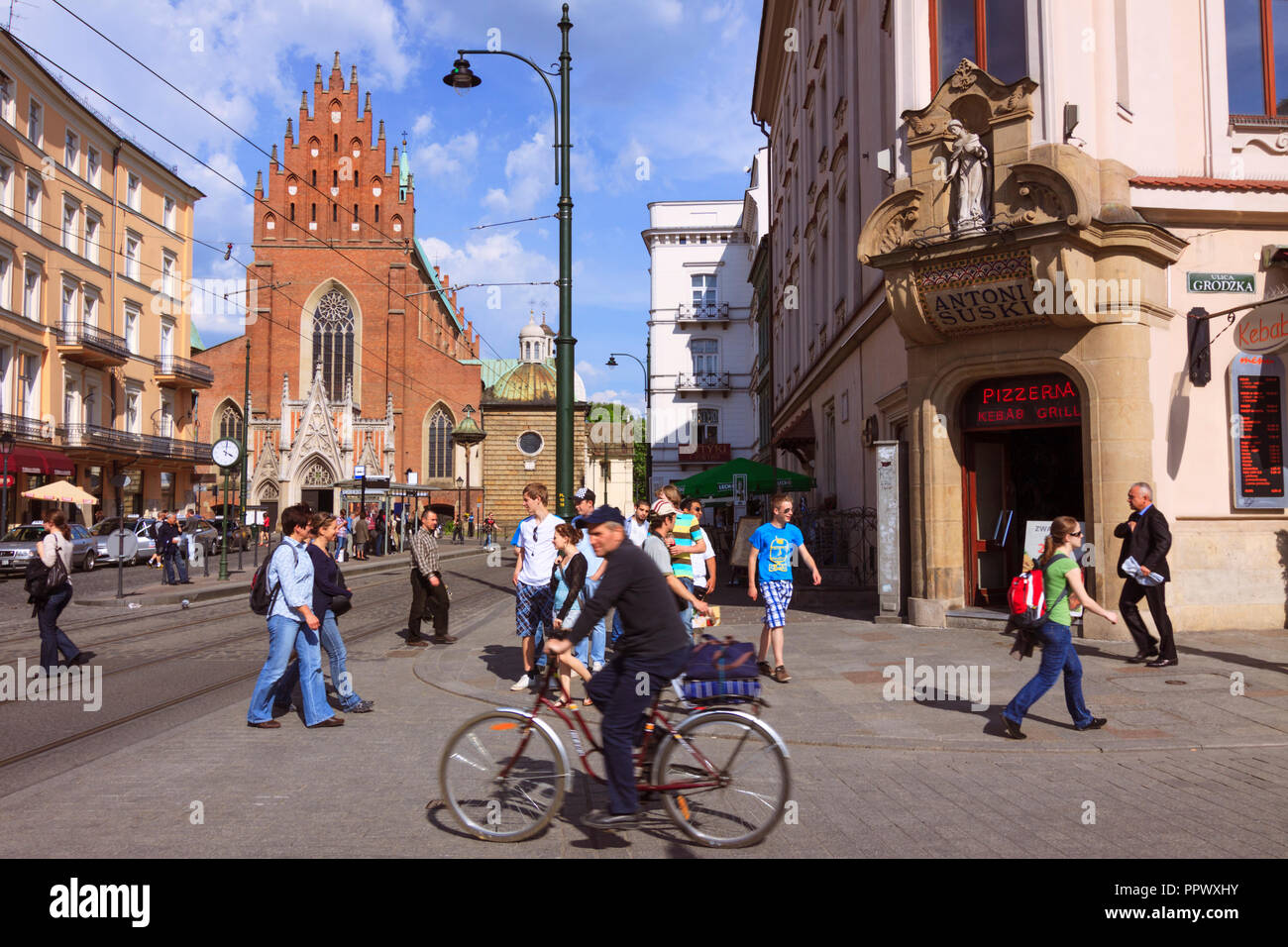 Cracovia, Polonia : gente a pie y en bicicleta en la calle Grodzka, listado  por la Unesco en la ciudad vieja. La iglesia de la santísima Trinidad en el  fondo Fotografía de