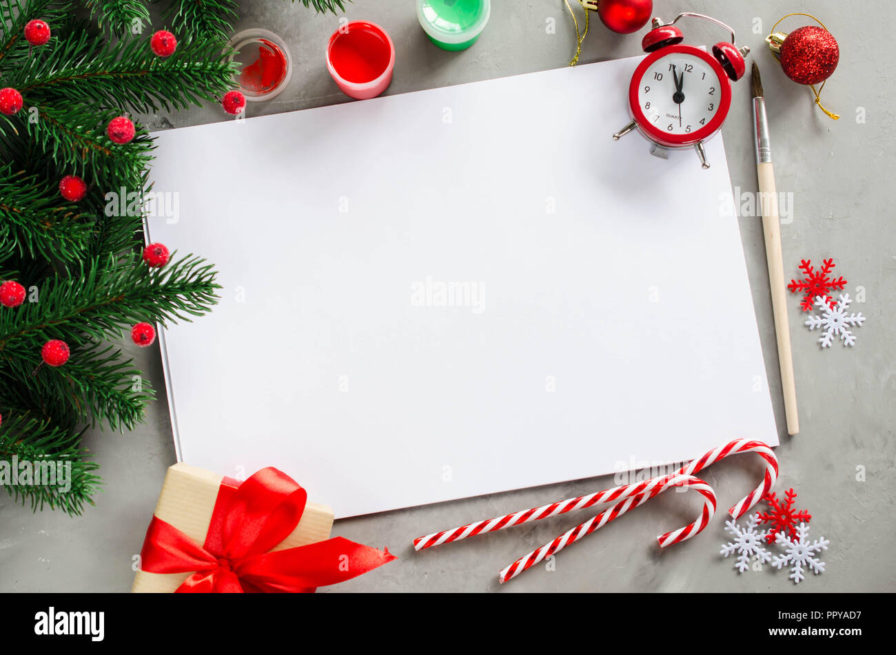 Maqueta de Navidad para la tarjeta de felicitación o carta a Papá Noel. Fondo  de navidad con papel blanco vacío, pinturas, ramas de abeto y despertador.  Vista desde arriba Fotografía de stock -