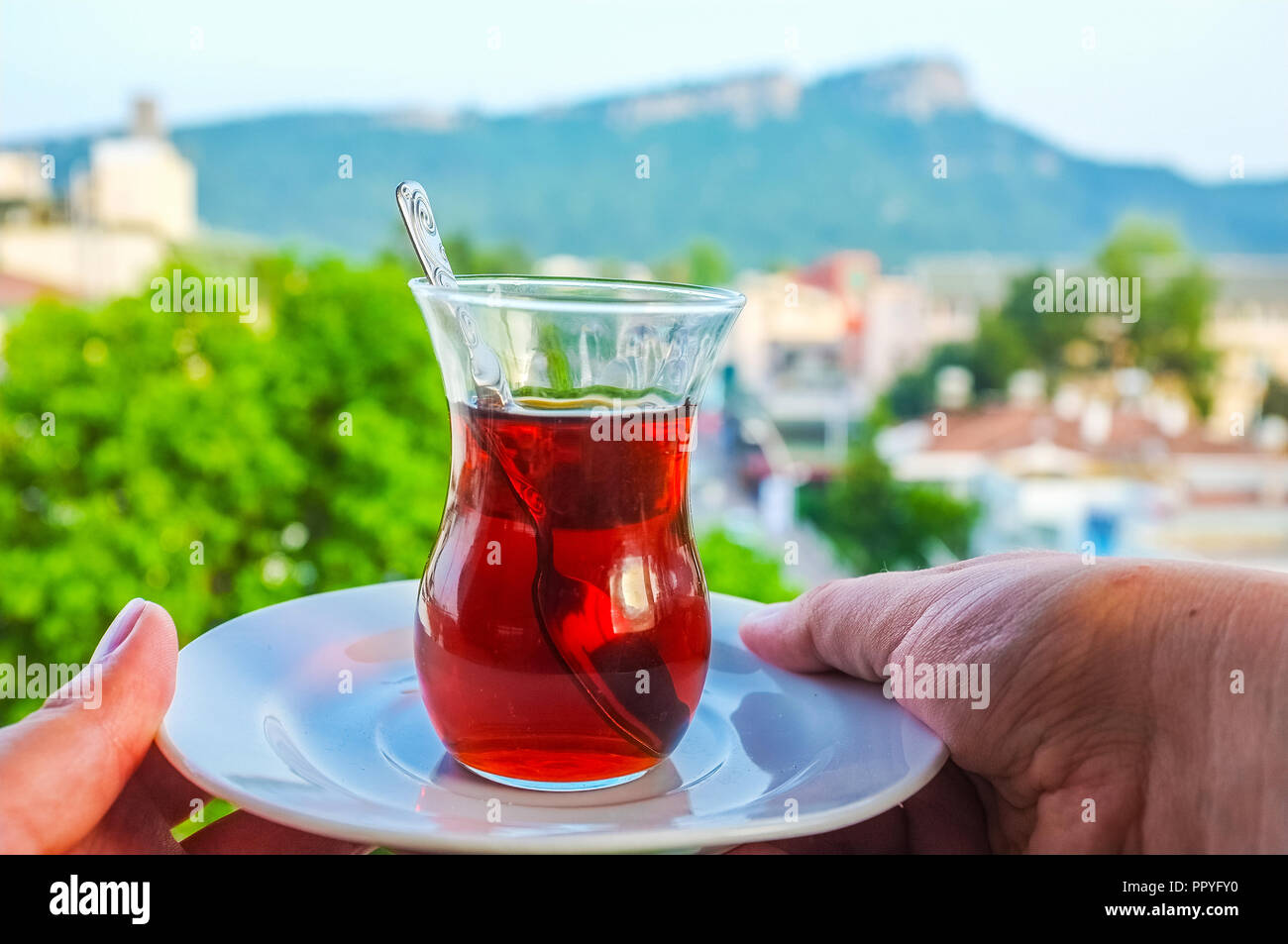 Agitación té turco negro en un vaso con una vista sobre las Montañas Tauro en Kemer, Turquía. Foto de stock