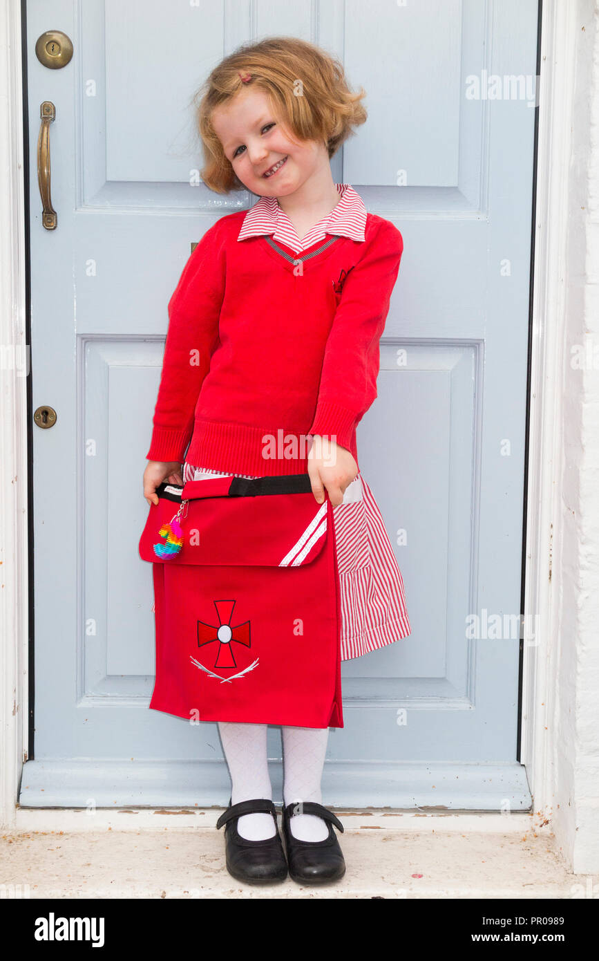 Cuatro años, alumna de la escuela / niña / niño / cabrito en nuevo uniforme en su puerta, salir de casa para ir a la escuela en su 1ª / primer día de escuela. En el Reino Unido. Foto de stock