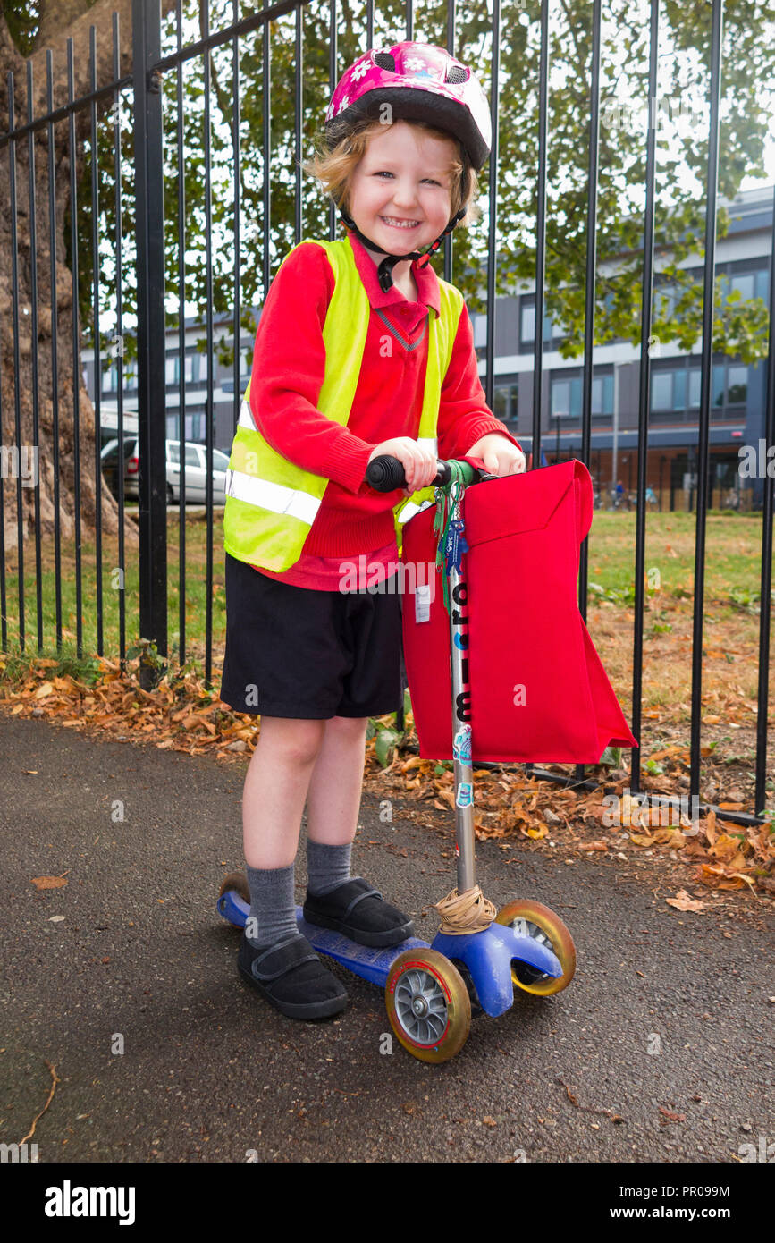 Niño de 4 años en scooter / chica en su hi vis / chaleco de alta visibilidad El scootering a casa de la escuela clases de recepción. En el Reino Unido. (102) Foto de stock