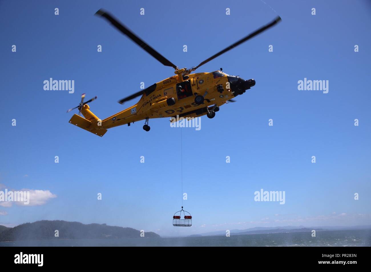 Una tripulación a bordo de un helicóptero MH-60 Jayhawk de Guardacostas Río Columbia Sector reduce un canasto de rescate durante ejercicios de entrenamiento de rutina en el Río Columbia, cerca de Ilwaco, Washington, 3 de julio de 2018. Una canasta de rescate es uno de los equipos más utilizados por la tripulación. La Guardia Costera de EE.UU. Foto por Petty oficial de 2ª clase Aaron Wills. Foto de stock