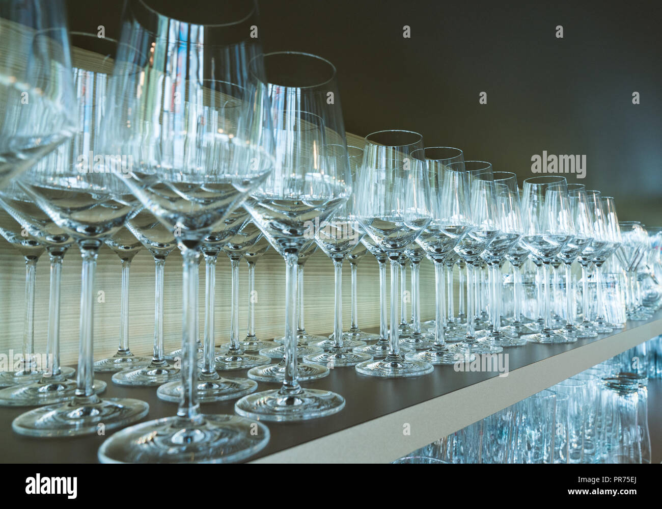 Fila interminable de copas de vino cuidadosamente apilados en un estante de madera en un restaurante bar Foto de stock